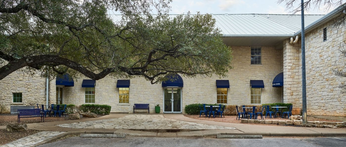 Front entrance of Austin International School, a limestone building with blue awnings and an oak tree